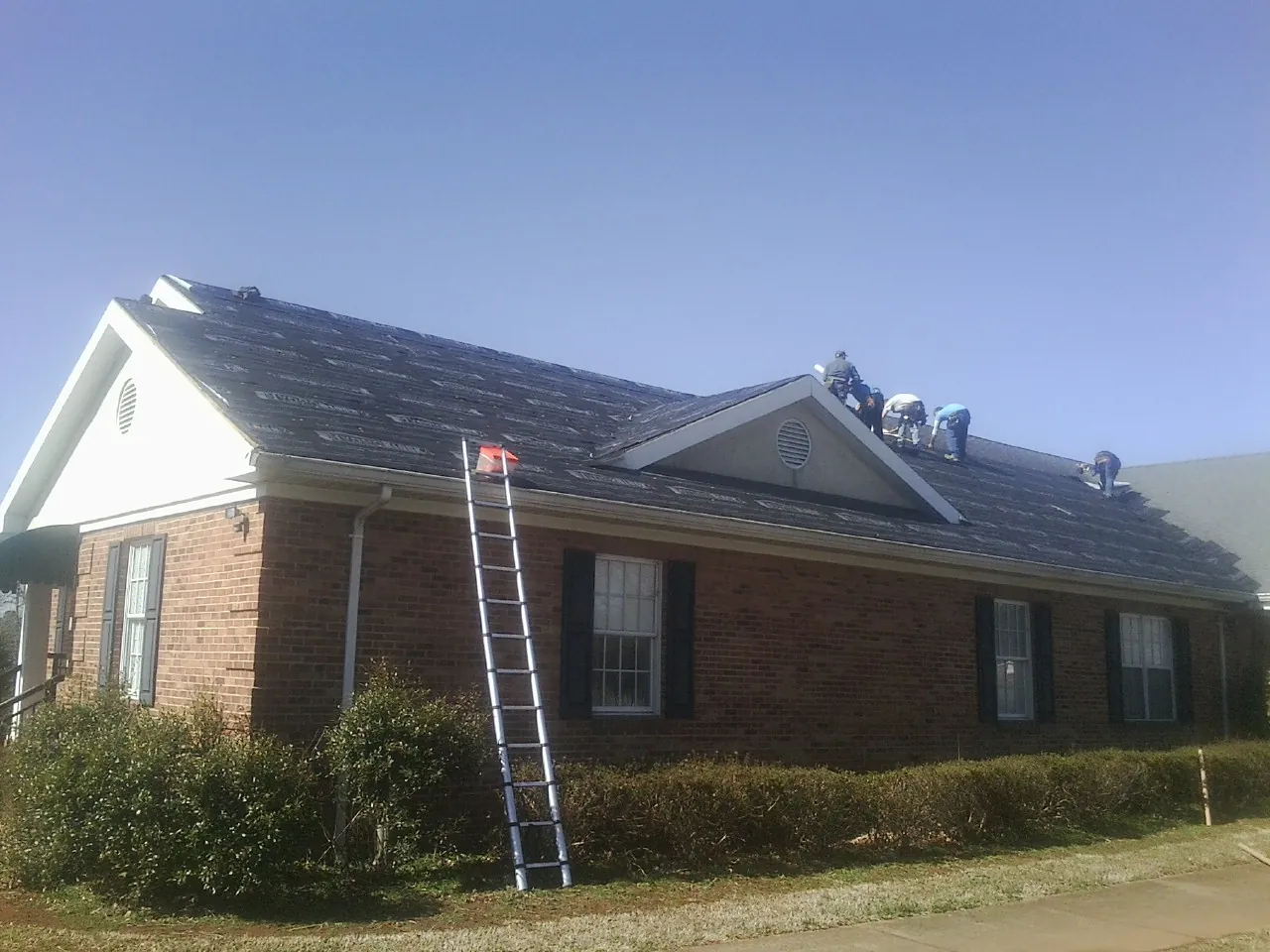 Crew tearing shingles off a brick ranch roof with a ladder set — Emergency Roof Repair work by our crew in Buzzards Bay