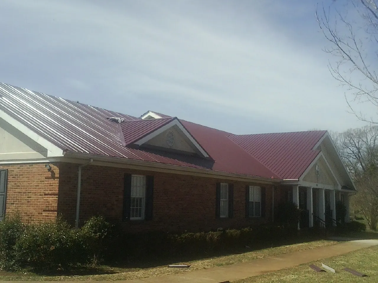 Red metal roof with gabled entries on a long brick building, from a Hail Damage Roof Repair job in Buzzards Bay