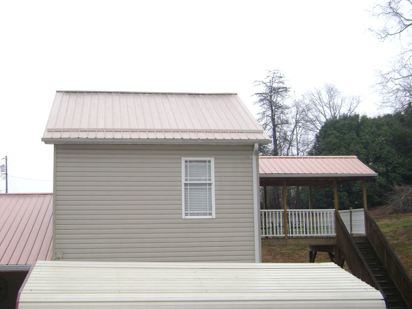 Tan metal roofs on a two story addition and attached porch, from a Roof Replacement job in Buzzards Bay